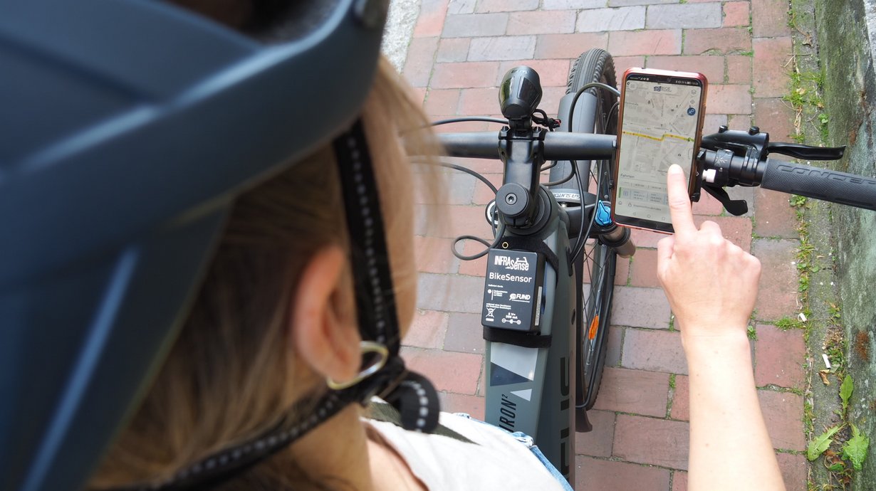 Eine Radfahrerin, die den Infrasense-Sensor an ihrem Fahrrad montiert hat, betrachtet die Daten in der BIQEmonitor-App. 
